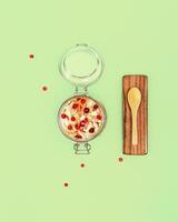 Fermented cabbage with cranberries and spices in a glass jar, wooden spoon on a white background photo