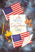 Withe sheet with kid drawing and inscription Happy Columbus Day, american flags, paper boat and autumn leaves photo