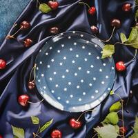 Empty blue plate with a star pattern and cherry berries with leaves on a satin fold fabric photo