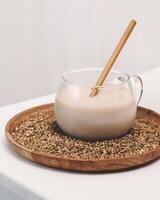 Glass cup of plant milk with wooden straw on a wooden plate with buckwheat groats photo