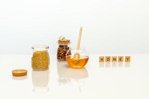 Natural bee products in glass jars and a wooden inscription honey on a white table photo