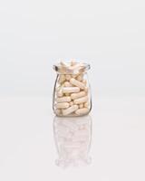 White capsules in a glass bottle on a white table photo