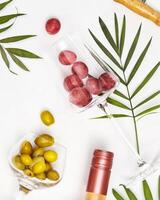 Wine glasses with grapes and green olives, bottle of rose wine and palm leaves photo