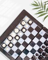 Chess board with placed pieces and palm leaves on a blue background photo