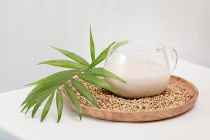 Glass cup of plant milk with palm leaf on a wooden plate with buckwheat groats photo