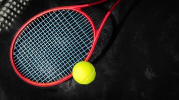 Yellow tennis ball with red racket on a black background with copy space photo