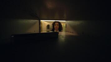 A woman peers curiously into a dark mailbox tunnel in a lowlight, mysterious setting video