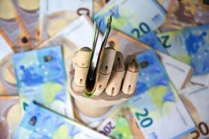 A wooden hand holds a stack of twenty Euro banknotes against a backdrop of additional twenty Euro notes photo