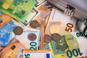 Close-up view of various Euro banknotes and coins, with a US dollar bill peeking out, scattered on a table, seemingly spilled from a metal case with a lock photo