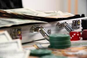 A close-up image of a silver suitcase open on a table with cash, a red dice, and stacks of poker chips photo
