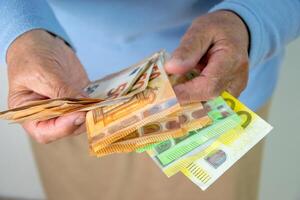 A person is holding a stack of euro banknotes in their hand. The bills are folded and fanned out, with the 50 euro note visible on top photo