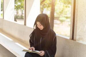 A beautiful Muslim students are intently reading Quran in the school building during breaks time in university with sun fare and blurred background. photo