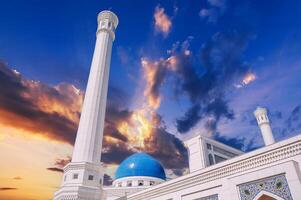 high white minaret and blue dome of modern Islamic Masjid Minor Mosque in Tashkent in Uzbekistan on background of sunset sky photo