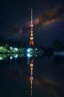 landmark television TV tower illuminated at night in Tashkent in Uzbekistan with a reflection in water of river on background of a starry sky with milky way photo