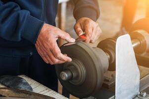male sharpener grinder sharpens a knife blade on sharpening machine with rotating abrasive wheel close-up photo