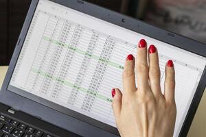 Close up shot of the woman with beautiful hands and manicure, working on the laptop, scrolling touch screen with mortgage loan amortization table open. Banking photo