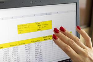 Close up shot of the woman with beautiful hands and manicure, working on the laptop, scrolling touch screen with mortgage loan amortization table open. Finance photo