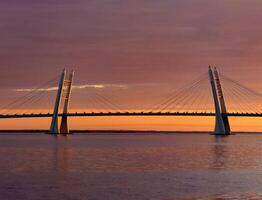 A breathtaking view of a cable-stayed bridge during a stunning sunset, with vibrant colors reflecting on calm waters. The dramatic sky adds to the beauty and serenity of the scene. photo