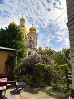 Scenic view of the golden domes of the Cathedral of the Vladimir Icon of the Mother of God, framed by lush greenery and a blooming garden in St. Petersburg. Perfect for travel, architecture, and religious-themed projects. photo