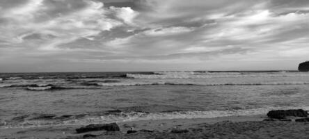 A black and white photo of a beach with waves crashing into the shore