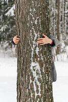 A person lovingly embraces a tree in a snowy forest, showing care for nature on Earth Day photo