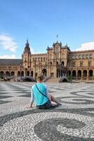 Back view of solo traveler girl sitting on the square of Spain in Seville. Backview of woman tourist in Sevilla trip. Solo vacation concept. photo