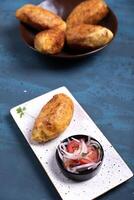 Top view of a crispy potato with a salty filling inside, accompanied by an onion and tomato salad. photo