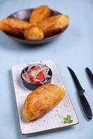 Top view of a crispy potato with a salty filling inside, accompanied by an onion and tomato salad. photo