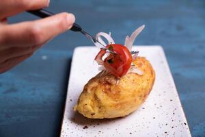 Hands with a fork putting salad on top of a stuffed potato. photo