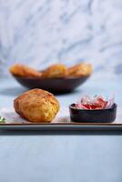 Front view of a crispy potato with a meat filling inside, accompanied by an onion and tomato salad. photo