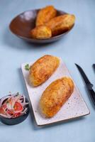 Appetizing Peruvian starter crispy stuffed potatoes on a plate, accompanied by an onion and tomato salad. photo