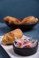 Top view of a crispy potato with a meat filling inside, accompanied by an onion and tomato salad. photo