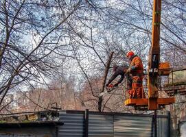 Dnepr, Ukraine - 03.20.2024 Municipal service workers stand with a chainsaw in a crane basket and trim dangerous trees photo