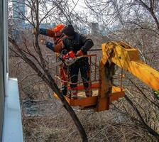Dnepr, Ukraine - 03.20.2024 Municipal service workers stand with a chainsaw in a crane basket and trim dangerous trees photo