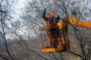 Dnepr, Ukraine - 03.20.2024 Municipal service workers stand with a chainsaw in a crane basket and trim dangerous trees photo