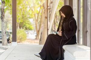 Side view of Muslim student wearing traditional clothes sit and review the lesson on tablet for the exam in university with sun fare and blurred background. photo