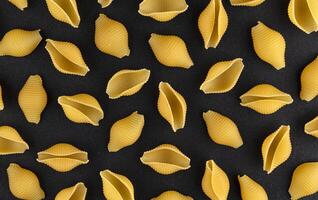 Dry shell pasta pattern on black background, top view photo