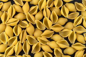 Dry shell pasta pattern on black background, top view photo