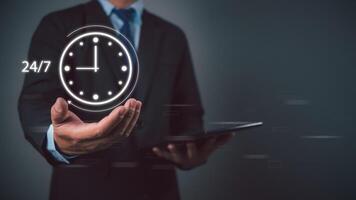 Businessman showing a symbol work 24 hour and 7 day by icon virtual screen hologram, 24 hour open, 24 hour payment online banking, shopping, transaction online service server cloud running. photo
