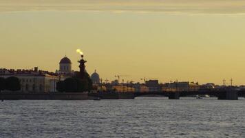 Scenic view of the iconic Rostral Column with a flame at its top, set against the backdrop of historical buildings in Saint Petersburg during sunset. The Neva River in the foreground enhances the tranquil atmosphere. video