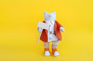 A soft toy cat with a wooden sign with a place for text, on a yellow background. photo