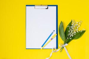 A tablet with paper as a template with a place to copy on a yellow table with lilies of the valley photo