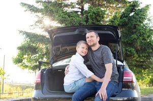 Dad and son are sitting in the trunk of a car at sunset. Hugging Dad and laughing photo