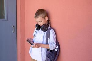 Cute boy playing on the phone. A child goes home from school with a backpack. photo