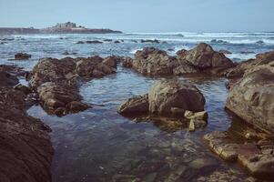 Scenic view of rocky shoreline with tidal pools and waves under a clear blue sky photo