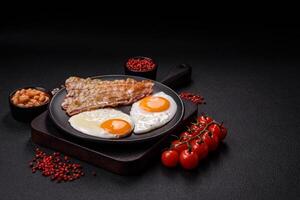 English breakfast with fried eggs, bacon, beans, tomatoes, spices and herbs photo