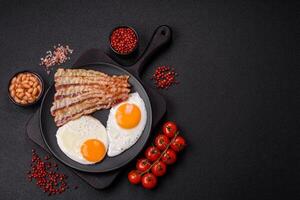 English breakfast with fried eggs, bacon, beans, tomatoes, spices and herbs photo