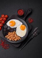 English breakfast with fried eggs, bacon, beans, tomatoes, spices and herbs photo