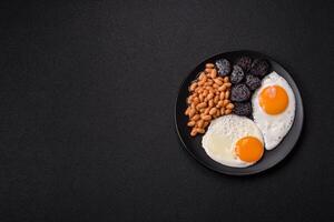 English breakfast with fried eggs, bacon, beans, tomatoes, spices and herbs photo