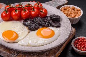 English breakfast with fried eggs, bacon, beans, tomatoes, spices and herbs photo